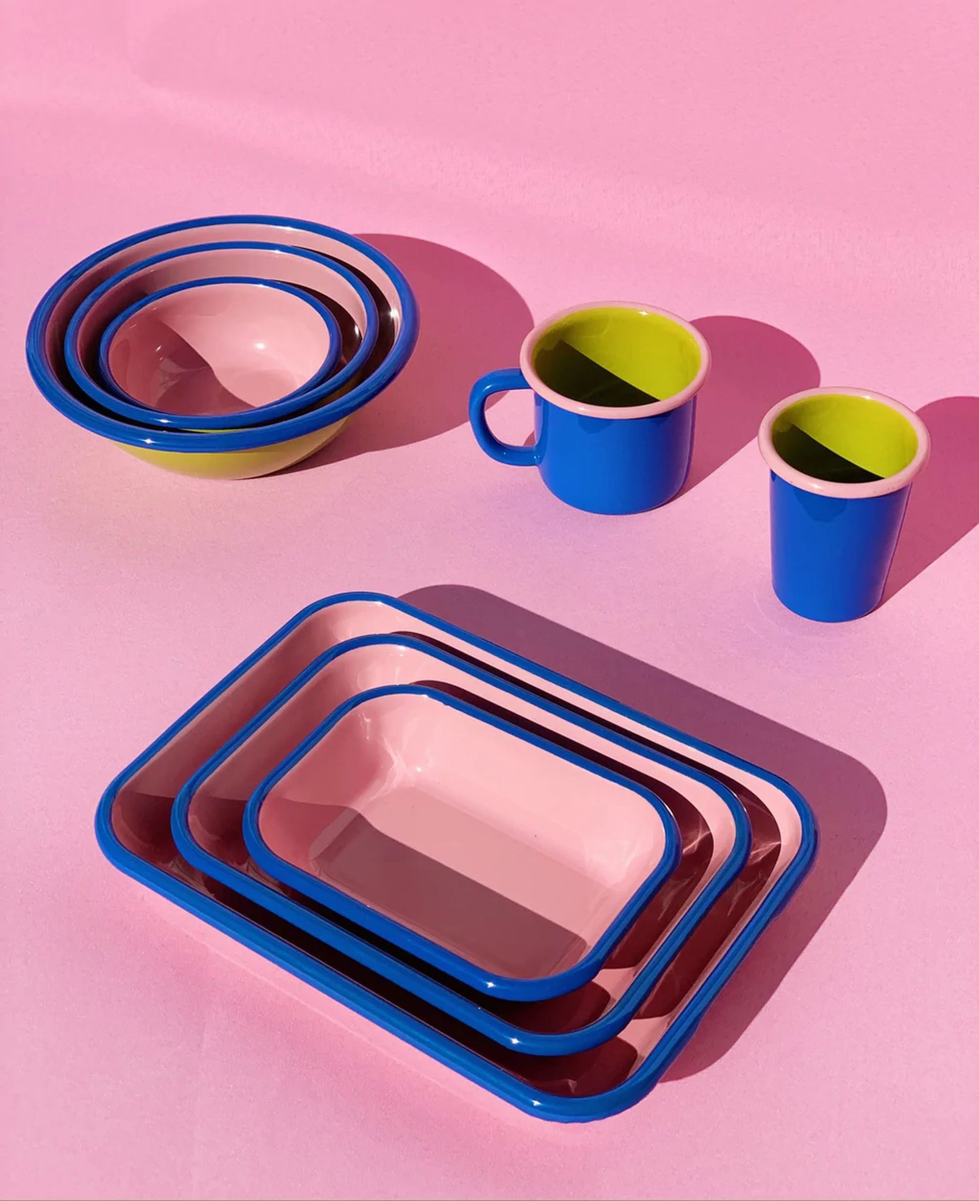 A set of colorful Bornn Enamelware Colorama Baking Dishes (Medium) by Bornn Enamelware sits on a pink surface, featuring vibrant handmade design and adding a playful touch to your table setting.