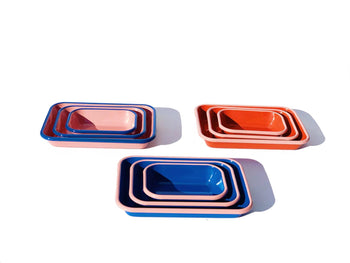 The Bornn Enamelware Colorama Baking Dish (Medium) is shown stacked in pink, orange, and blue on a white background, highlighting the brand’s unique handmade design.