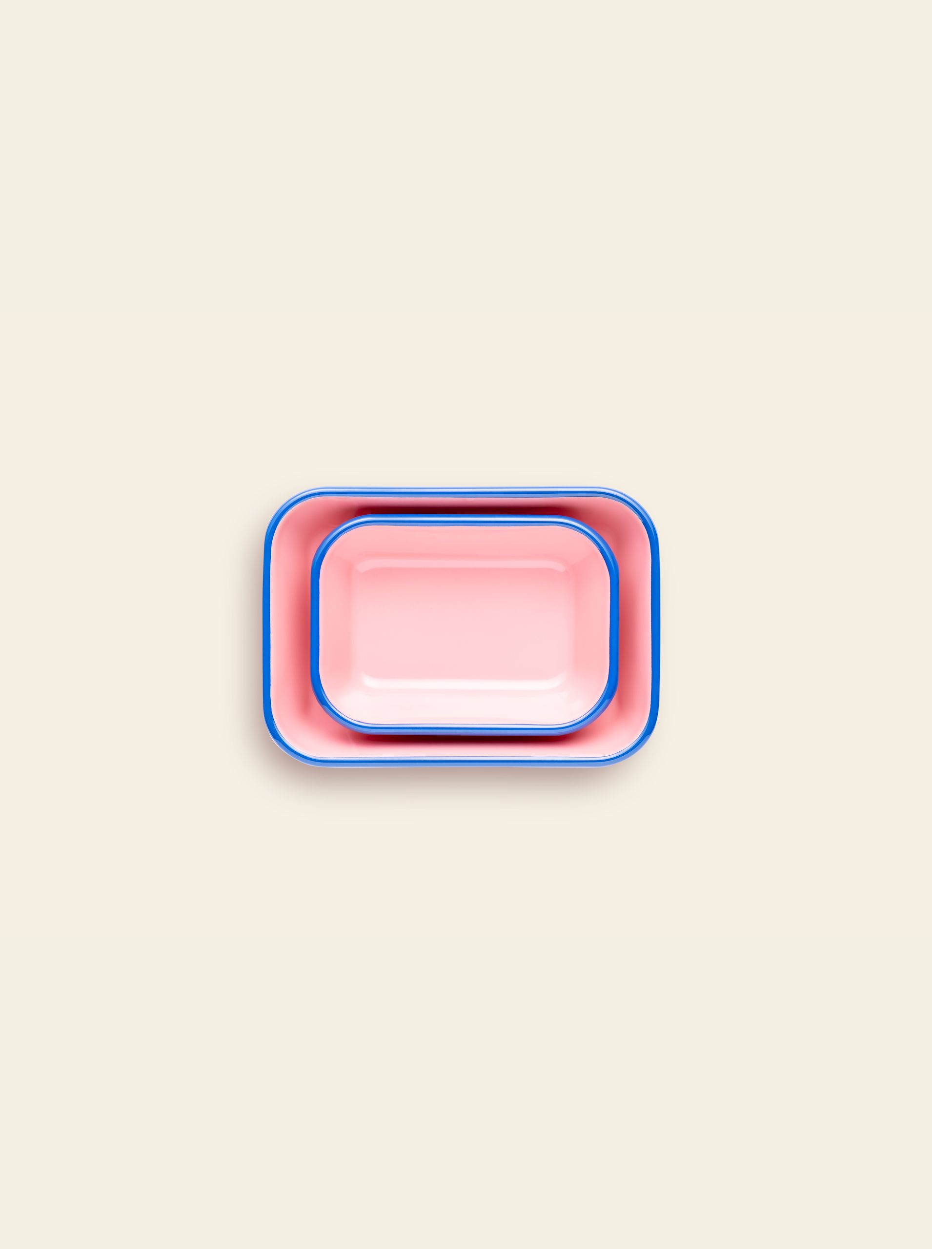Two rectangular pink Bornn Enamelware Colorama Baking Dishes with blue rims, one nested in the other, display their vibrant handmade style on a light beige background.