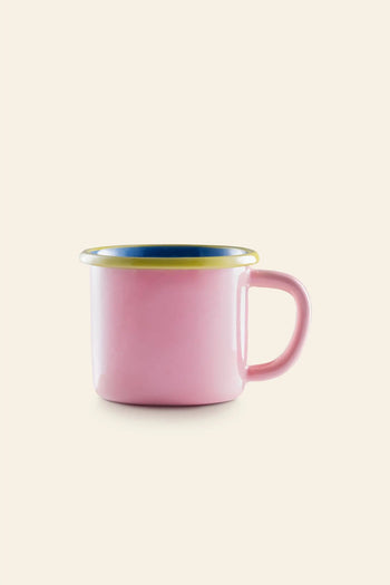 The Bornn Enamelware Colorama Mug by Bornn Enamelware features a pink enamel finish, wide handle, blue interior, and yellow rim—making it ideal for your morning coffee. Displayed against a light beige background.