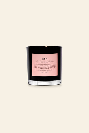 The Boy Smells Ash Scented Candle 8.5oz features a black glass vessel with a pink label, offering notes of lemon peel and dry hay—a perfect addition to any nature lovers candle collection.