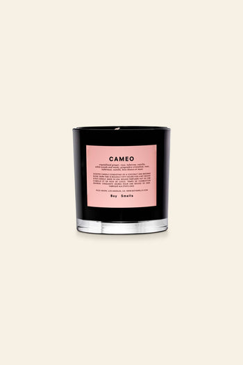 The Boy Smells Cameo Scented Candle 8.5oz features a black glass jar with a pink label marked CAMEO, listing notes like crystallised ginger. It rests on a beige background, with the Boy Smells brand at the bottom of the label.