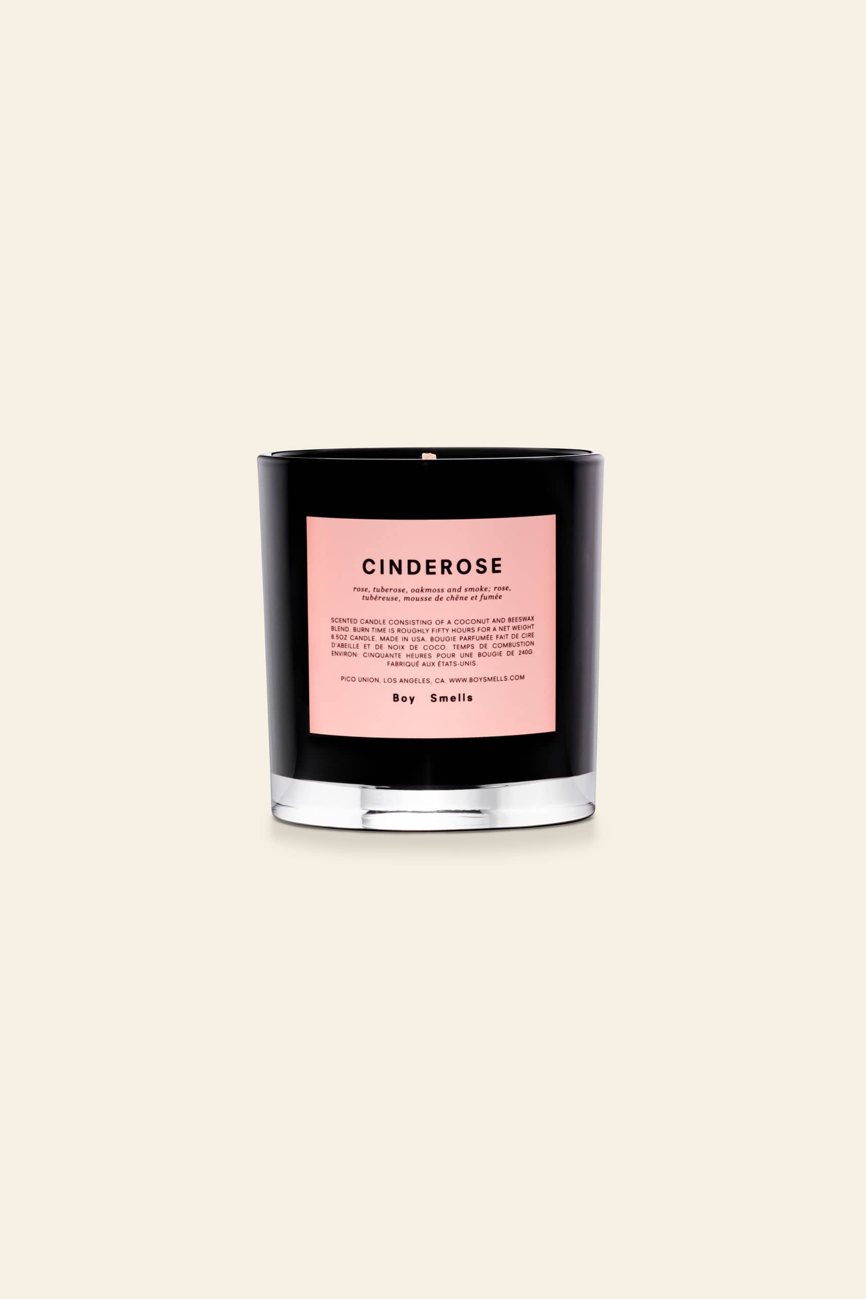 A black glass Boy Smells Cinderose Scented Candle 8.5oz with a pink label sits against a beige background. The unused candle, featuring an unlit wick, offers a delicate cinder rose floral fragrance.