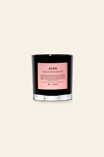 The Boy Smells Kush Scented Candle 8.5oz features a black glass jar with a pink label, set against a beige background, and evokes the essence of Kush with an herbal bouquet and subtle floral notes.