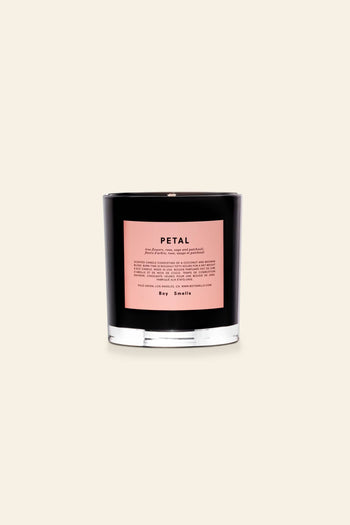The Boy Smells Petal Scented Candle 8.5oz features a black glass vessel with a pink label and black text. It sits on a light beige background and offers an enchanting scent of exotic musk and magnolia.
