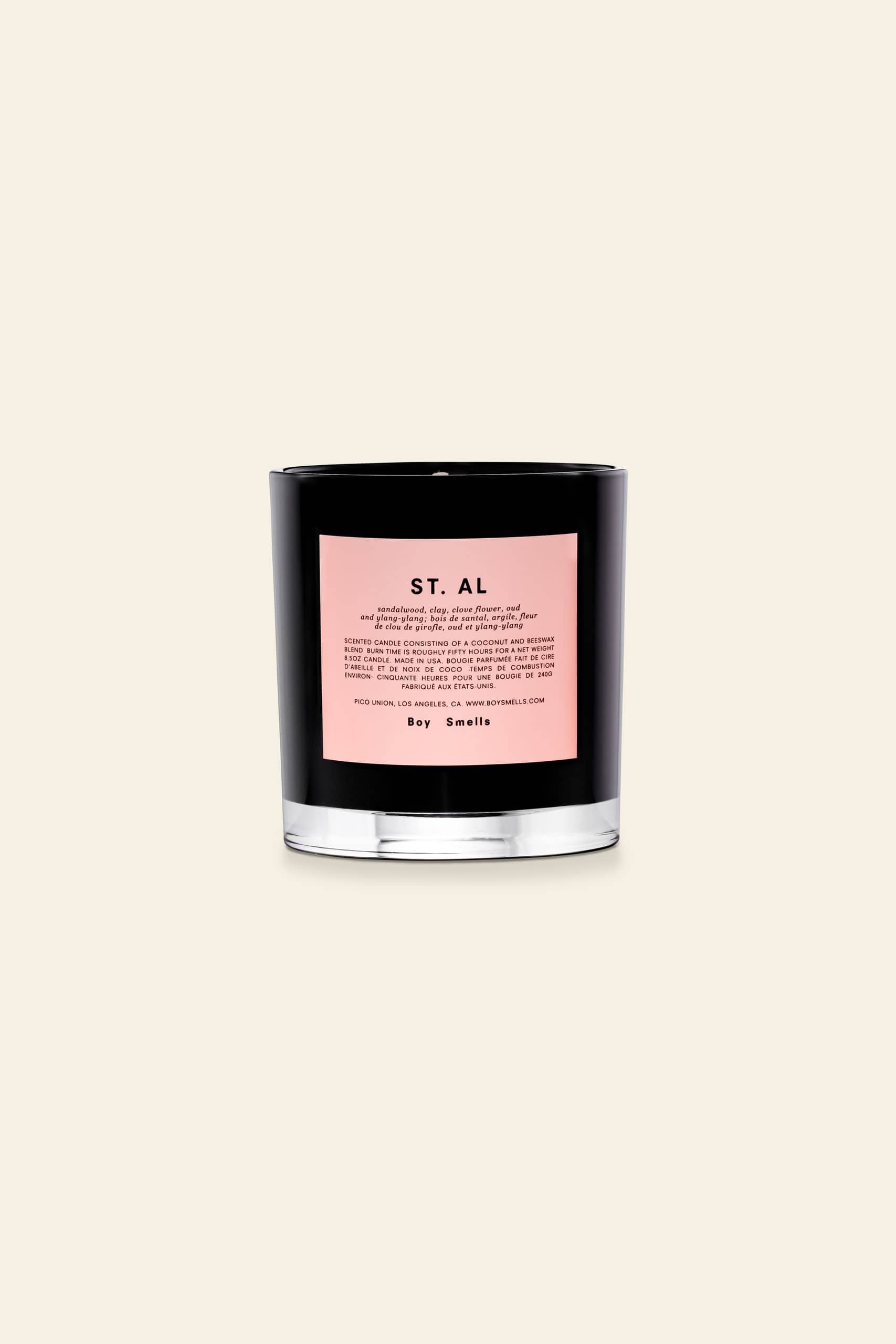 The Boy Smells St. Al Scented Candle 8.5oz features a black glass vessel with a pink label on a light beige background, releasing an inviting blend of sandalwood and exotic florals by Boy Smells.
