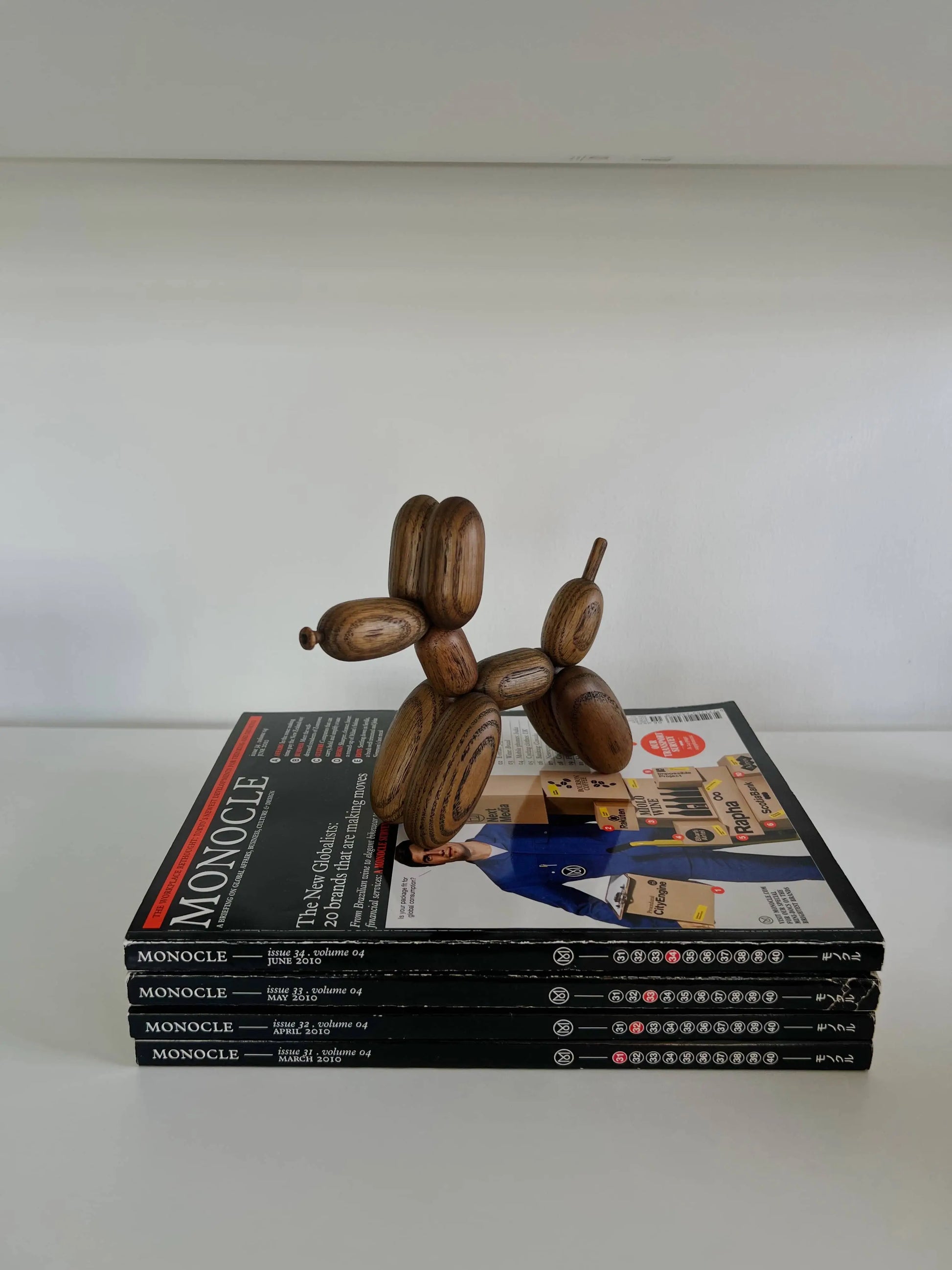 The Boyhood Ballon Dog Small by Boyhood, crafted from European FSC certified oak, sits atop a stack of five Monocle magazines on a white surface with a plain white background.
