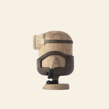 The Boyhood Minion Bob Small by Boyhood is a wooden figurine with a playful look, featuring a cylindrical body, one large round eye, black gloves and shoes. It’s displayed on a plain cream background and viewed from the side.