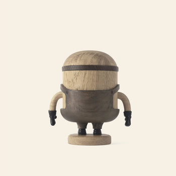 The Boyhood Minion Bob Small by Boyhood is a wooden figurine with a rounded head and body, small arms with black gloves, and a playful Minions-inspired look, standing on a circular base against a plain light background.