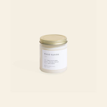 The Brooklyn Candle Studio Palo Santo Jar Candle, featuring a minimalist white label and gold metal lid, sits against a light beige background, inspired by the cleansing rituals of the sacred Palo Santo tree.