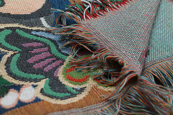 A close-up of the DETAIL Black Cat Oax Throwket by DETAIL highlights its vibrant artisanal design, featuring green, red, white, and black threads and detailed fringes with the intricate reverse side visible.