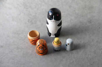 The DETAIL Feline 5 Nesting Dolls by DETAIL features five wooden dolls—a black-and-white cat, tiger, yellow chick, grey penguin, and more—displayed opened on a gray surface; ideal for cat lovers and collectors.