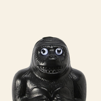 The DETAIL Gorilla Bank Small by DETAIL is a black figurine with large googly eyes and a toothy grin, set against a light beige background—a fun decorative accent for any room.