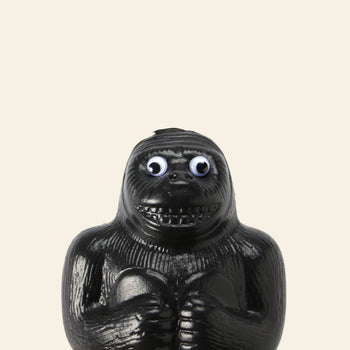 The DETAIL Gorilla Bank Small by DETAIL is a playful black plastic figurine with exaggerated features and googly eyes, standing upright against a light beige background—perfect as a fun decorative piece.