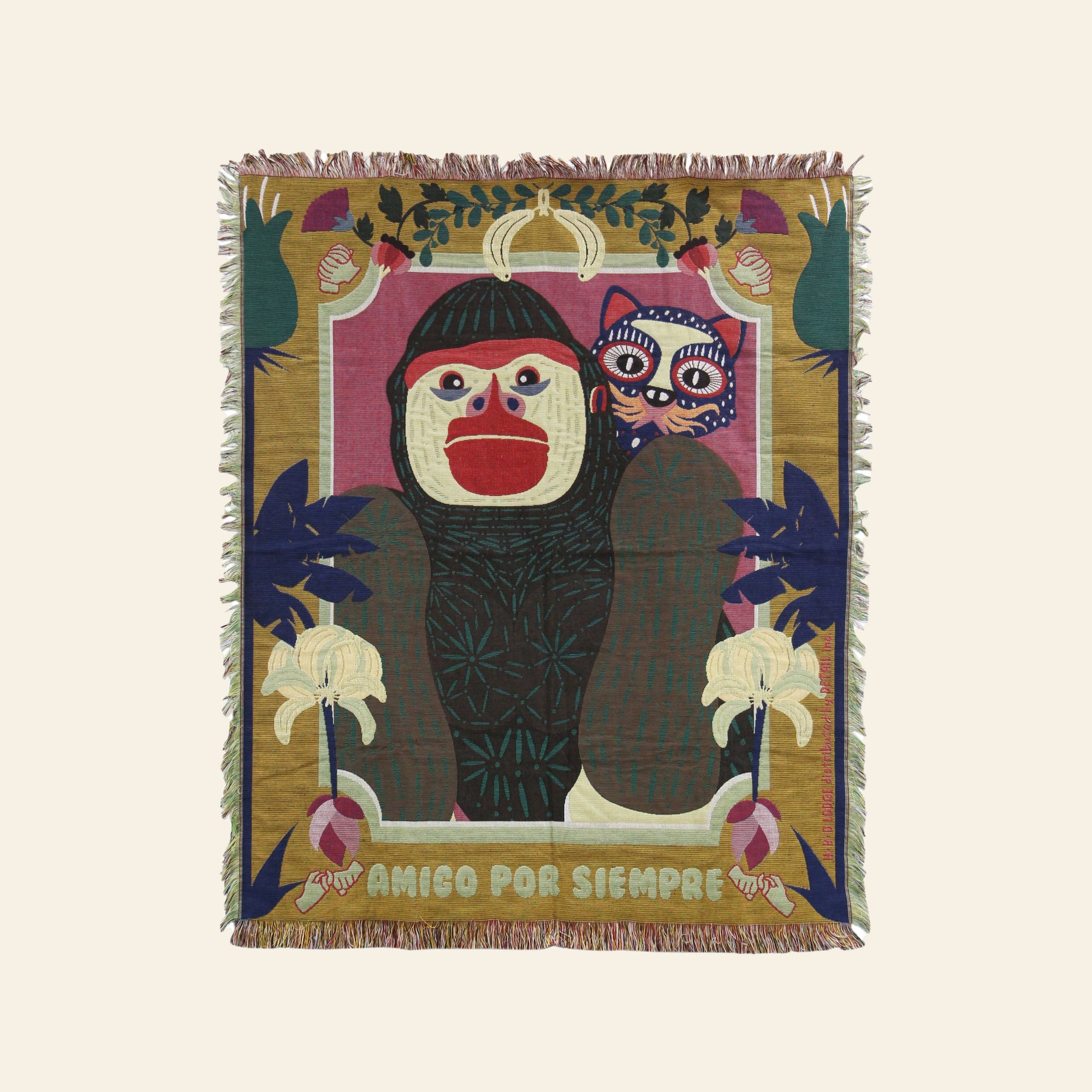 The DETAIL Gorilla Oax Throwket by DETAIL is a multicolour throw blanket inspired by Oaxaca folk art, featuring an illustrated monkey with a red mouth, a purple creature, bananas, leaves, and AMIGO POR SIEMPRE at the bottom.