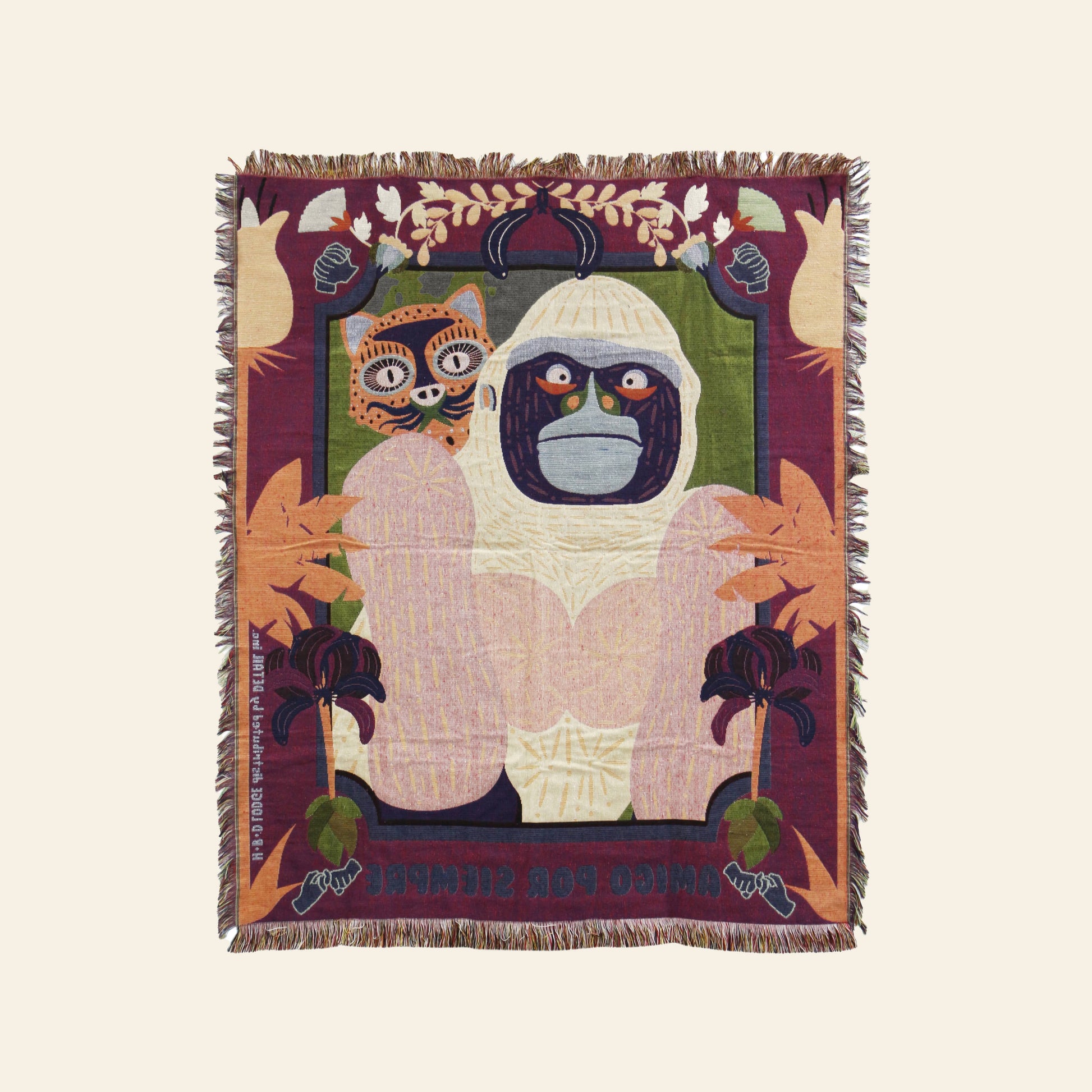 The DETAIL Gorilla Oax Throwket by DETAIL is a woven multicolour throw blanket with fringed edges, featuring a stylized white gorilla with a stern expression, Oaxaca folk art leaf motifs, a small cat-like face, and text at the bottom.