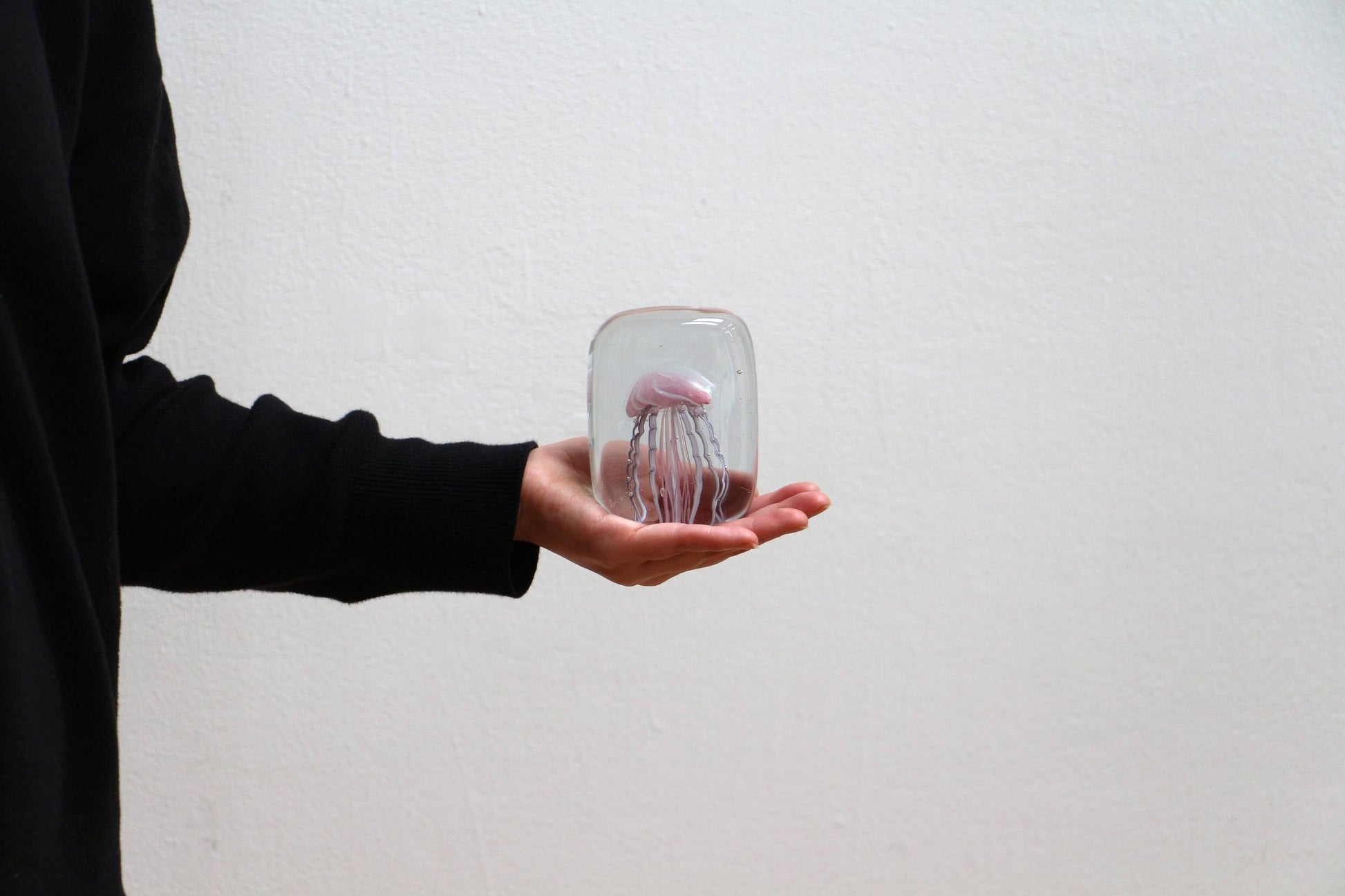 Someone wearing a black sleeve holds the DETAIL Jellyfish Twisted Leg Square paperweight by DETAIL, featuring an abstract jellyfish design, perfect for modern décor, against a plain white background.