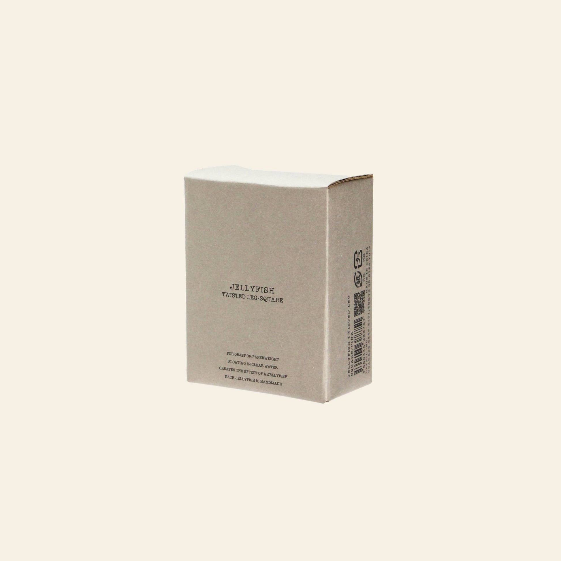 A plain, beige cardboard box labeled DETAIL Jellyfish Twisted Leg Square by DETAIL, featuring abstract jellyfish designs and a barcode on one side, stands upright against a light solid background—ideal for modern décor.