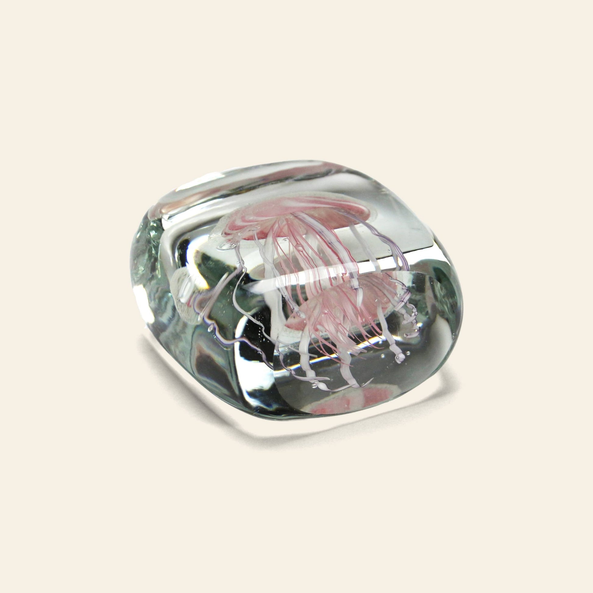 The DETAIL Jellyfish Twisted Leg Square by DETAIL is a clear glass paperweight featuring an abstract jellyfish design suspended inside, adding a modern décor touch against a light beige background.