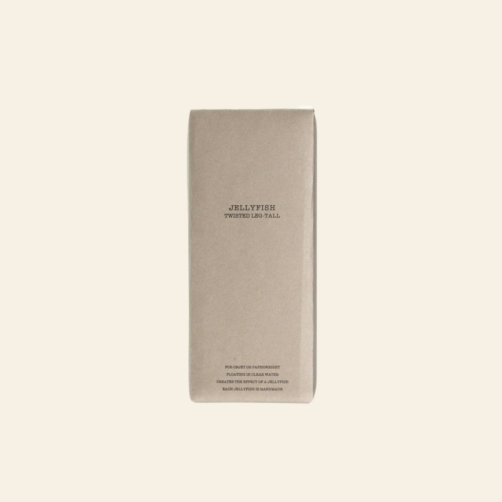 A rectangular, light brown cardboard box from DETAIL stands upright on a beige background. It’s labeled “DETAIL Jellyfish Twisted Leg Tall” in simple black text, hinting at the modern art glass sculpture inside.