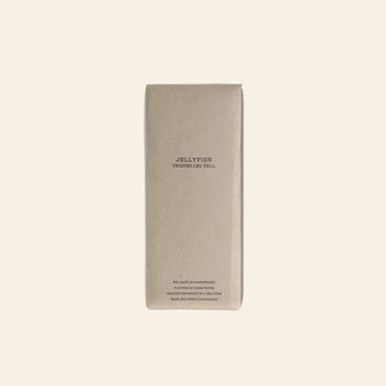 A rectangular, light brown cardboard box from DETAIL stands upright on a beige background. It’s labeled “DETAIL Jellyfish Twisted Leg Tall” in simple black text, hinting at the modern art glass sculpture inside.