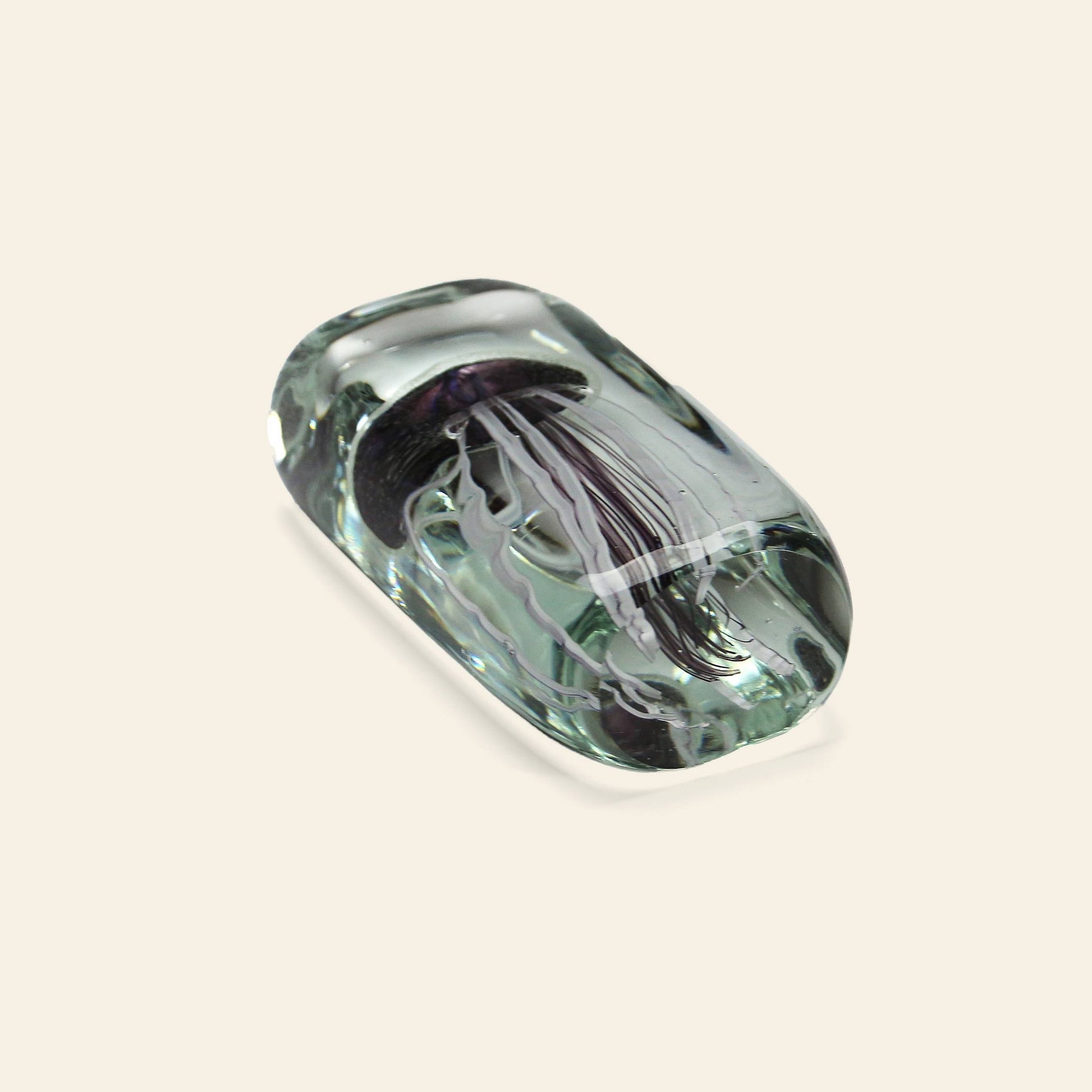 The DETAIL Jellyfish Twisted Leg Tall by DETAIL is a glass paperweight showcasing a lifelike jellyfish design suspended inside, elegantly displayed on a light beige background.