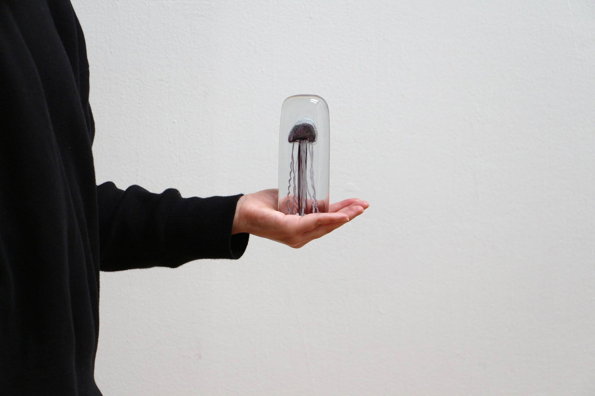 A person in a black long-sleeve top holds the DETAIL Jellyfish Twisted Leg Tall sculpture by DETAIL under a glass dome, creating a striking modern art display against a plain white background.