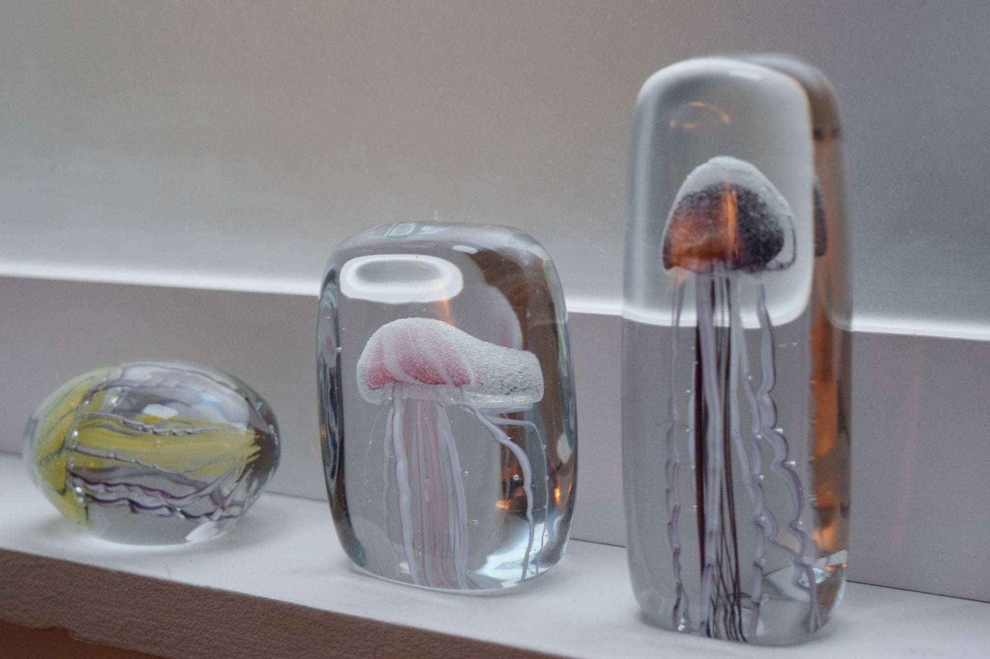 The DETAIL Jellyfish Twisted Leg Tall glass sculpture by DETAIL, with its vibrant, intricate design and tall cylinder shape, adds a modern artistic touch when displayed on a windowsill in soft light.