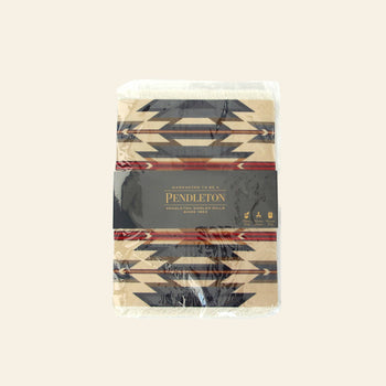 A DETAIL Mouse Rug Wyeth Trail by DETAIL, inspired by Native American carpet patterns, features a geometric black and beige design with original packaging and a dark label around the rug.