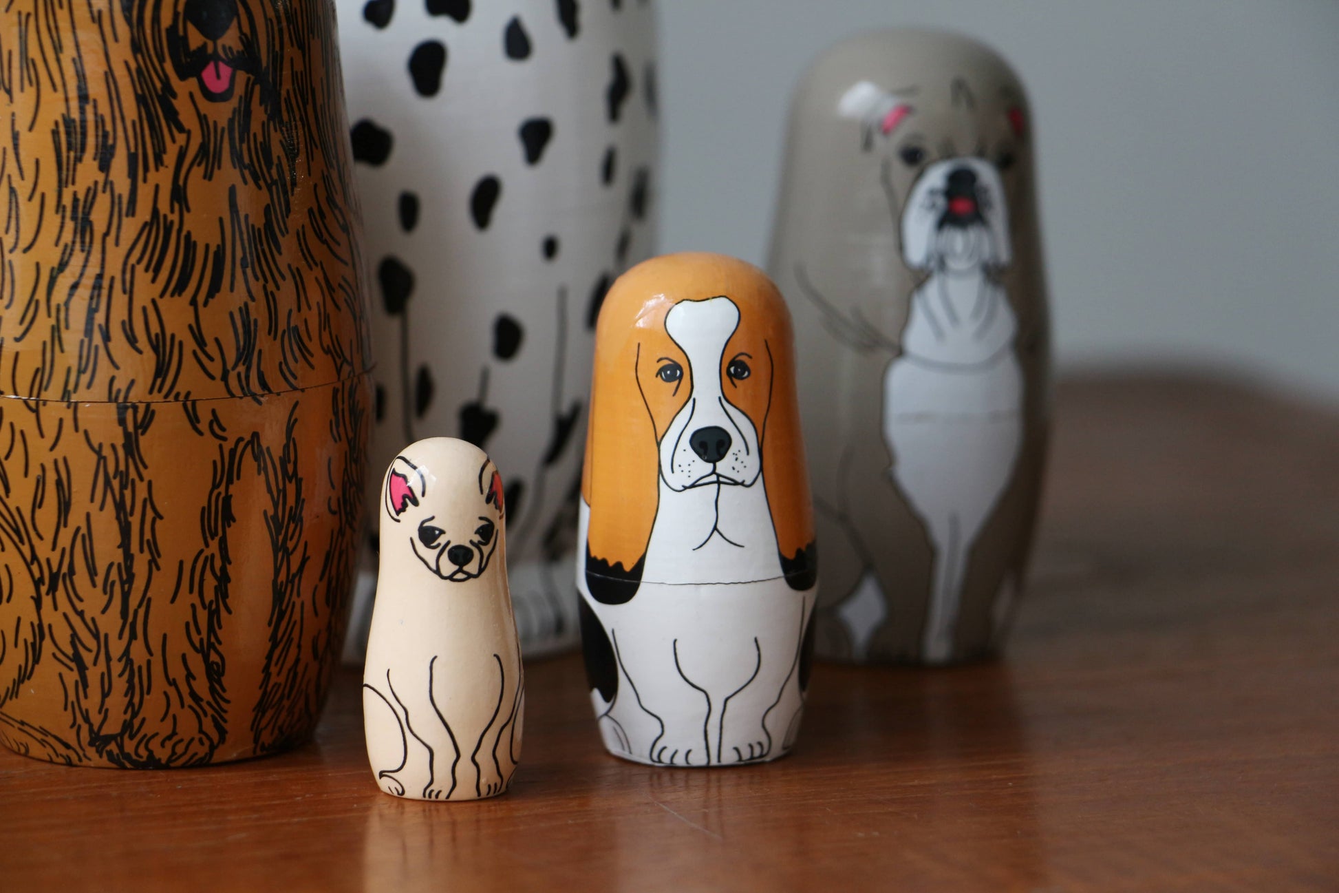 The DETAIL Partners Nesting Dolls by DETAIL feature five hand-painted wooden dolls, each with a unique dog design and fur pattern, showcasing different breeds and sizes lined up on a wooden surface.