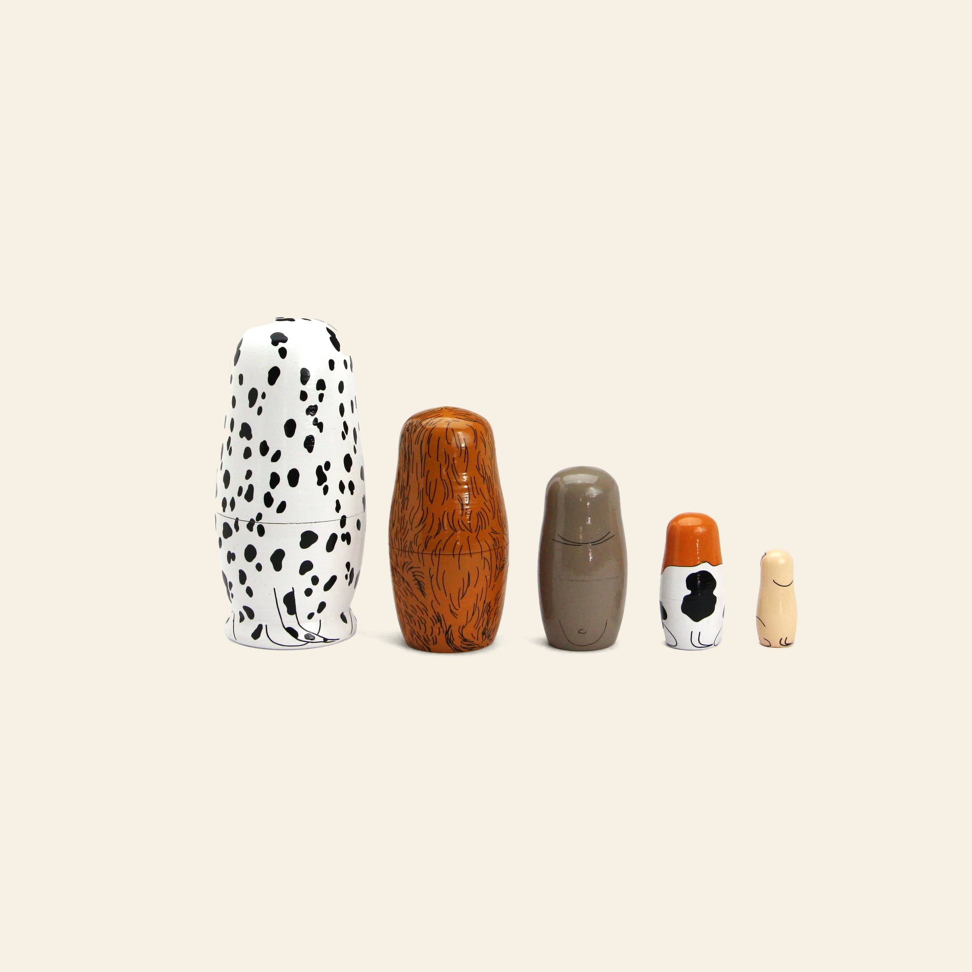DETAIL Partners Nesting Dolls by DETAIL: Five hand-painted wood nesting dolls, each with a unique dog design, are displayed in a row from largest to smallest on a light beige background.