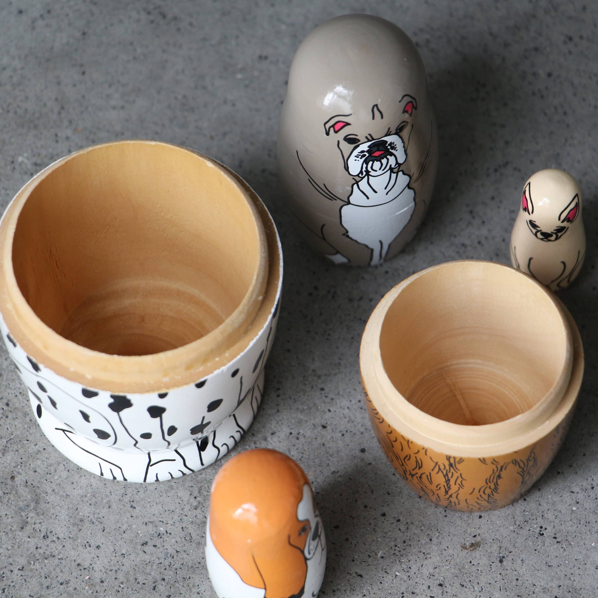 DETAIL Partners Nesting Dolls by DETAIL features four hand-painted wooden dolls, each with a unique dog design, displayed opened on a gray surface to show their inner and outer shells.
