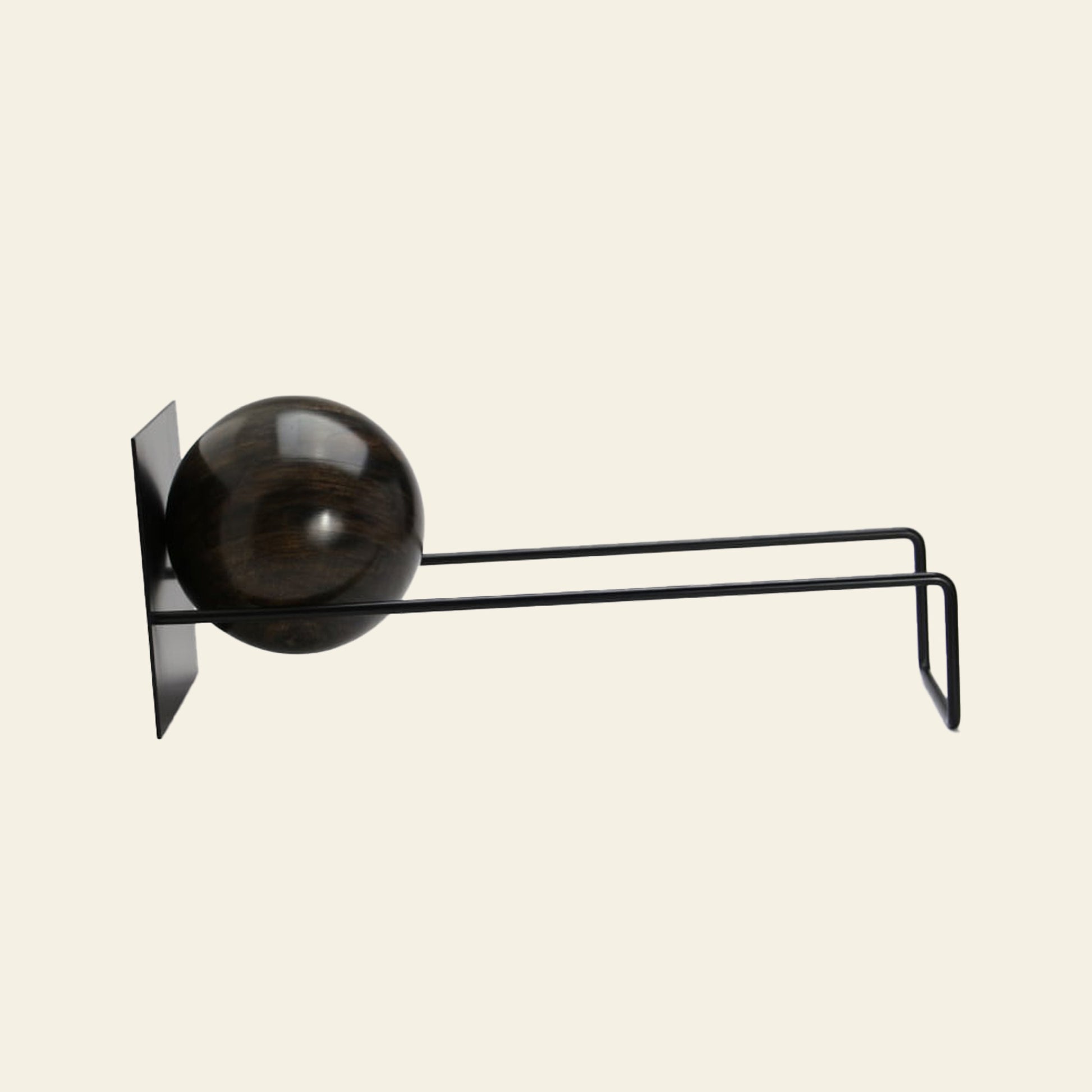 The DETAIL Slope Bookend by DETAIL features a modern, minimalist black design with dual parallel arms and a dark wooden sphere, reminiscent of a sculptural hook, styled against a simple light background.