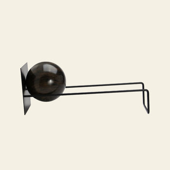 The DETAIL Slope Bookend by DETAIL features a modern, minimalist black design with dual parallel arms and a dark wooden sphere, reminiscent of a sculptural hook, styled against a simple light background.