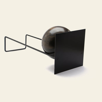 The DETAIL Slope Bookend by DETAIL features a dark wooden sphere partially encased in a black metal frame and flat black square panel, shown against a plain light background.