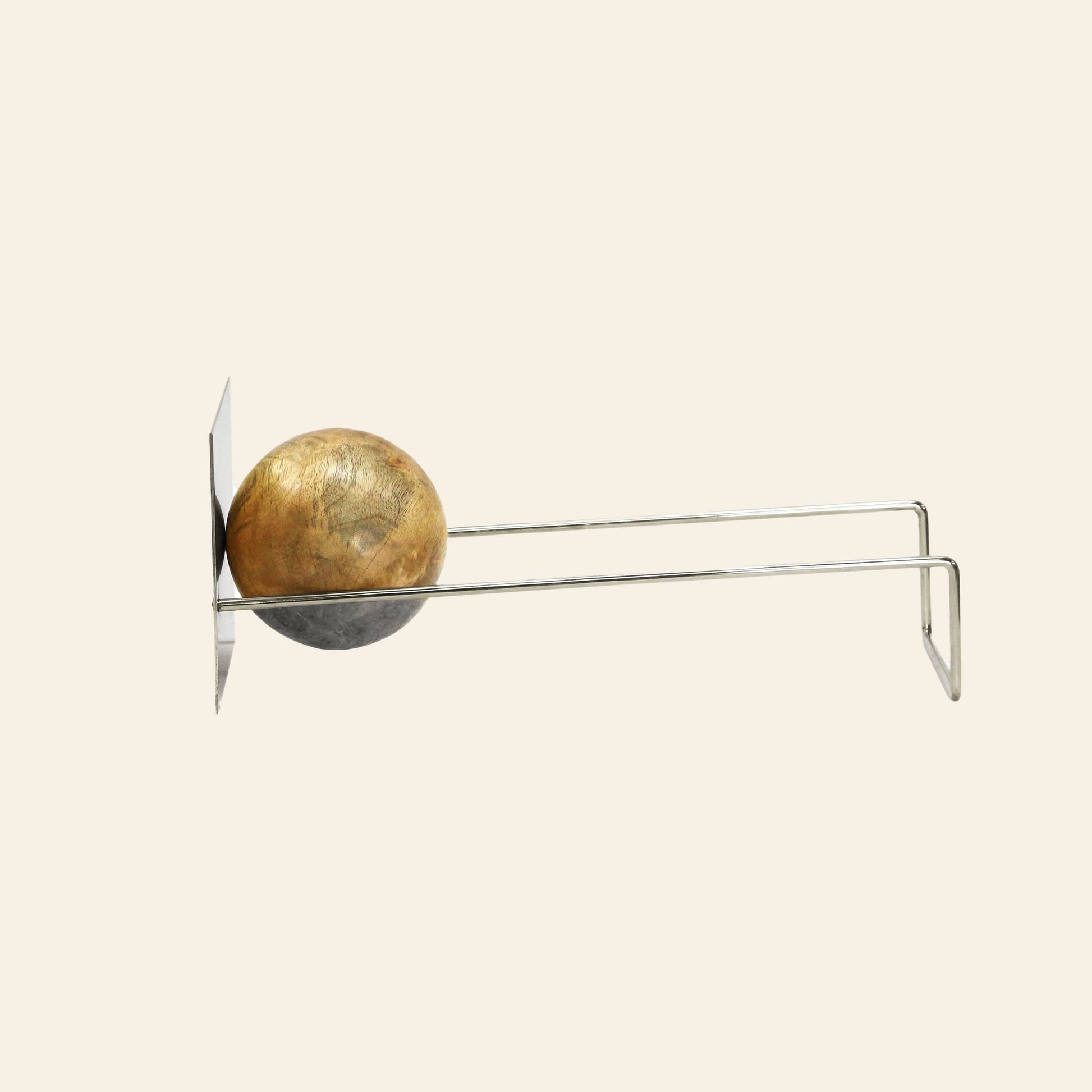 The DETAIL Slope Bookend by DETAIL is a minimalist wall-mounted sculptural bookend in silver, featuring a sphere held between two parallel rods that extend horizontally from a flat rectangular base.