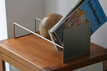The DETAIL Slope Bookend by DETAIL holds magazines and a decorative wooden globe on a wooden table near a white wall.