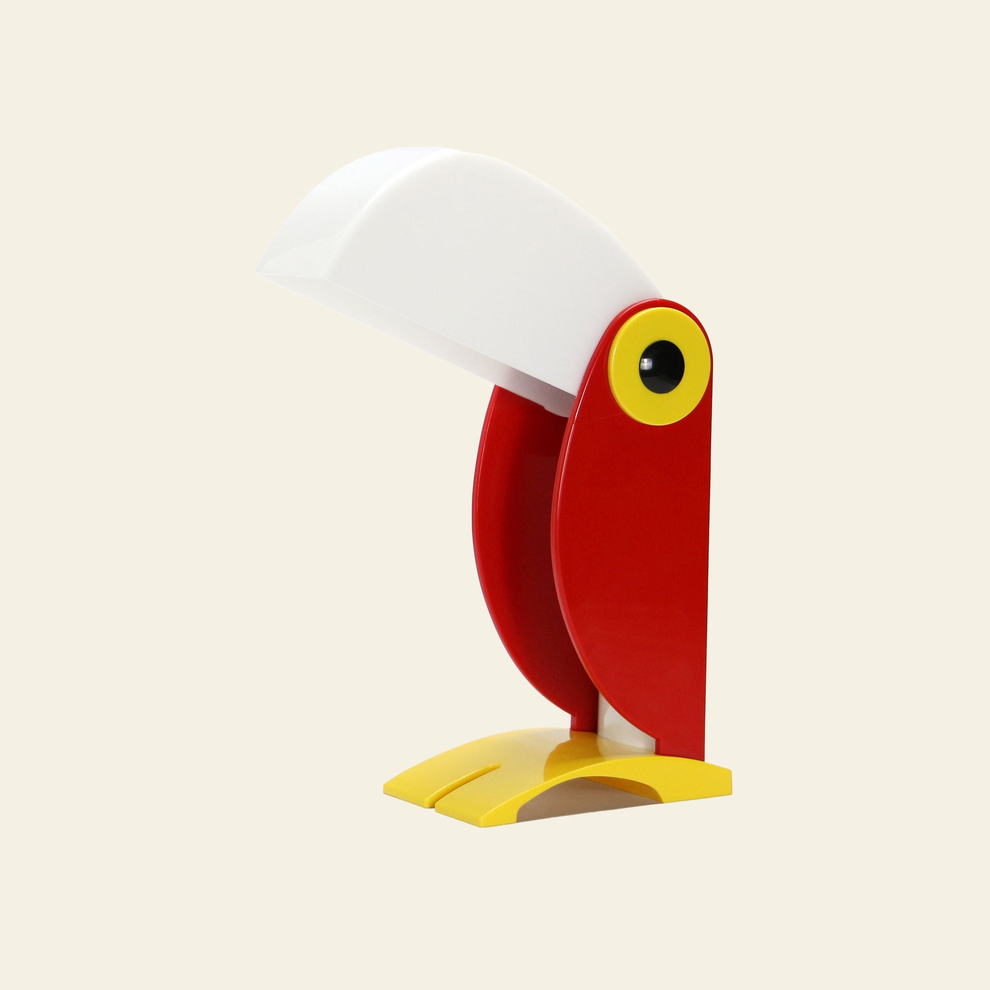 The DETAIL Toucan Lamp by DETAIL features vintage charm with a white beak-shaped shade, red body, yellow base and eye details, displayed against a plain light background.