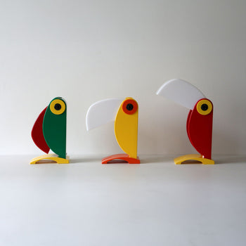 Three minimalist, colorful sculptures sit side by side, their geometric forms and angled beaks recalling the iconic design and vintage charm of the DETAIL Toucan Lamp by DETAIL.