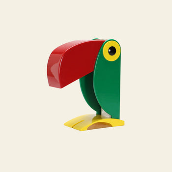 The DETAIL Toucan Lamp by DETAIL features a colorful, minimalist design with a large red beak, green body, yellow feet, and a yellow-rimmed eye, capturing iconic vintage charm against a plain light background.