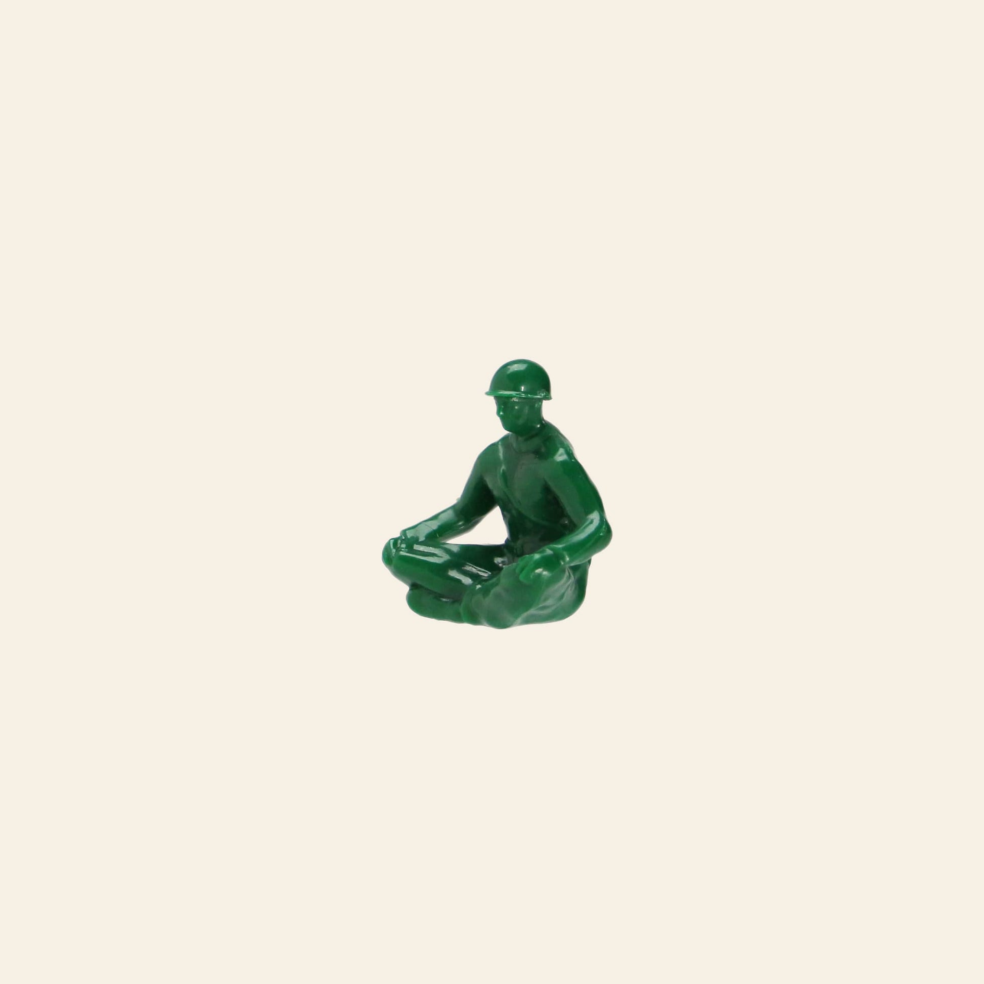 A DETAIL Yoga Joes 9 Figures toy by DETAIL shows a small green plastic soldier sitting cross-legged with a helmet, holding an object on his lap, set against a plain beige background.