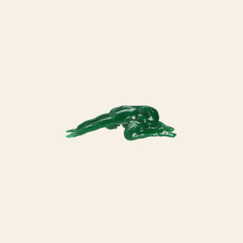 A small green plastic figure from the DETAIL Yoga Joes 9 Figures set by DETAIL lies face down, arms and legs extended like a soldier, against a plain off-white background.