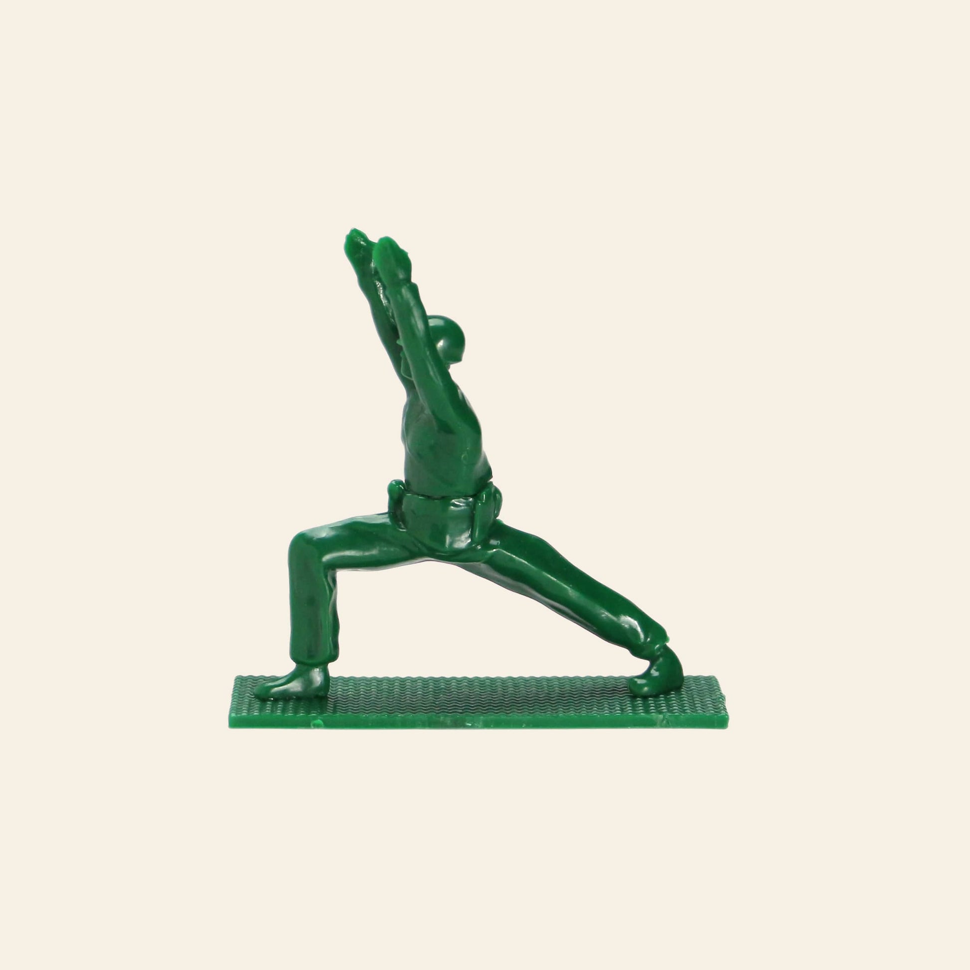 A green plastic DETAIL Yoga Joes soldier figure by DETAIL strikes a warrior yoga pose on a textured rectangular base, set against a plain beige background.
