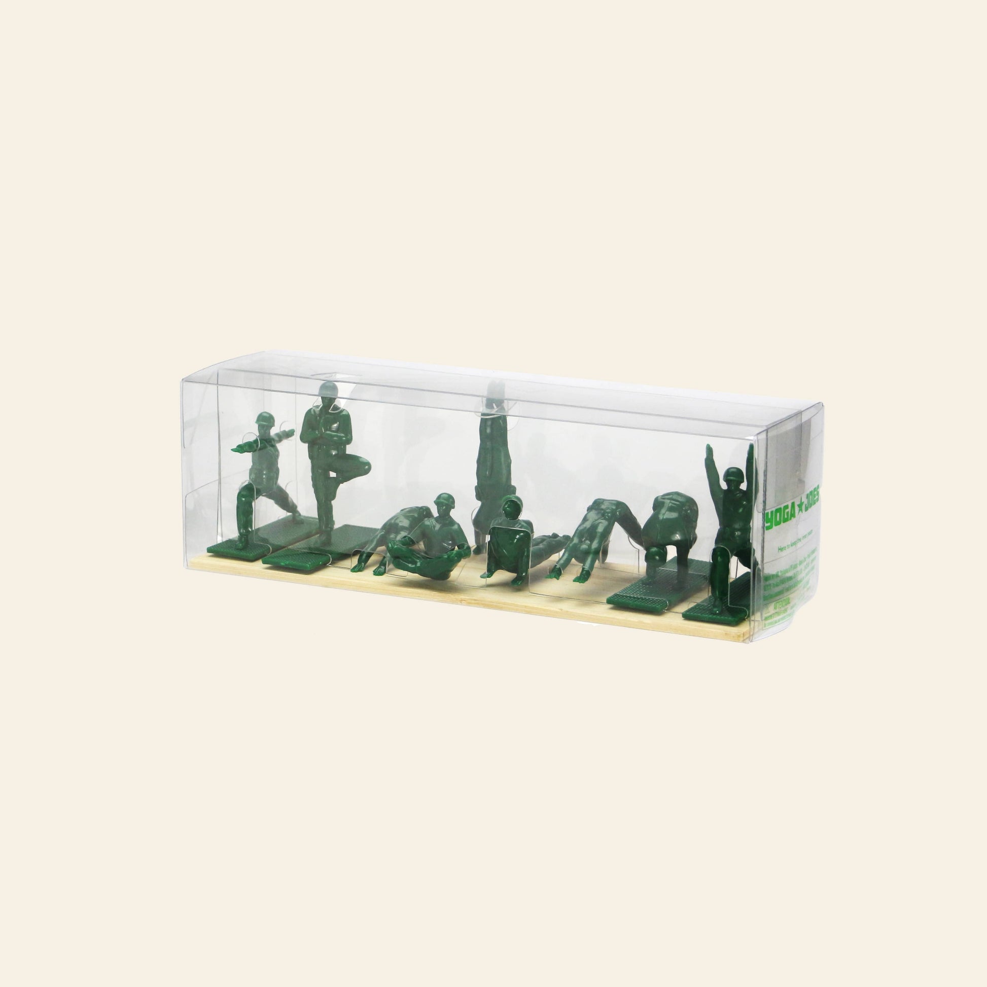 A clear plastic box showcases DETAIL Yoga Joes 9 Figures by DETAIL—green yoga figurines styled like toy soldiers, each striking a pose on a beige base against a plain light background.