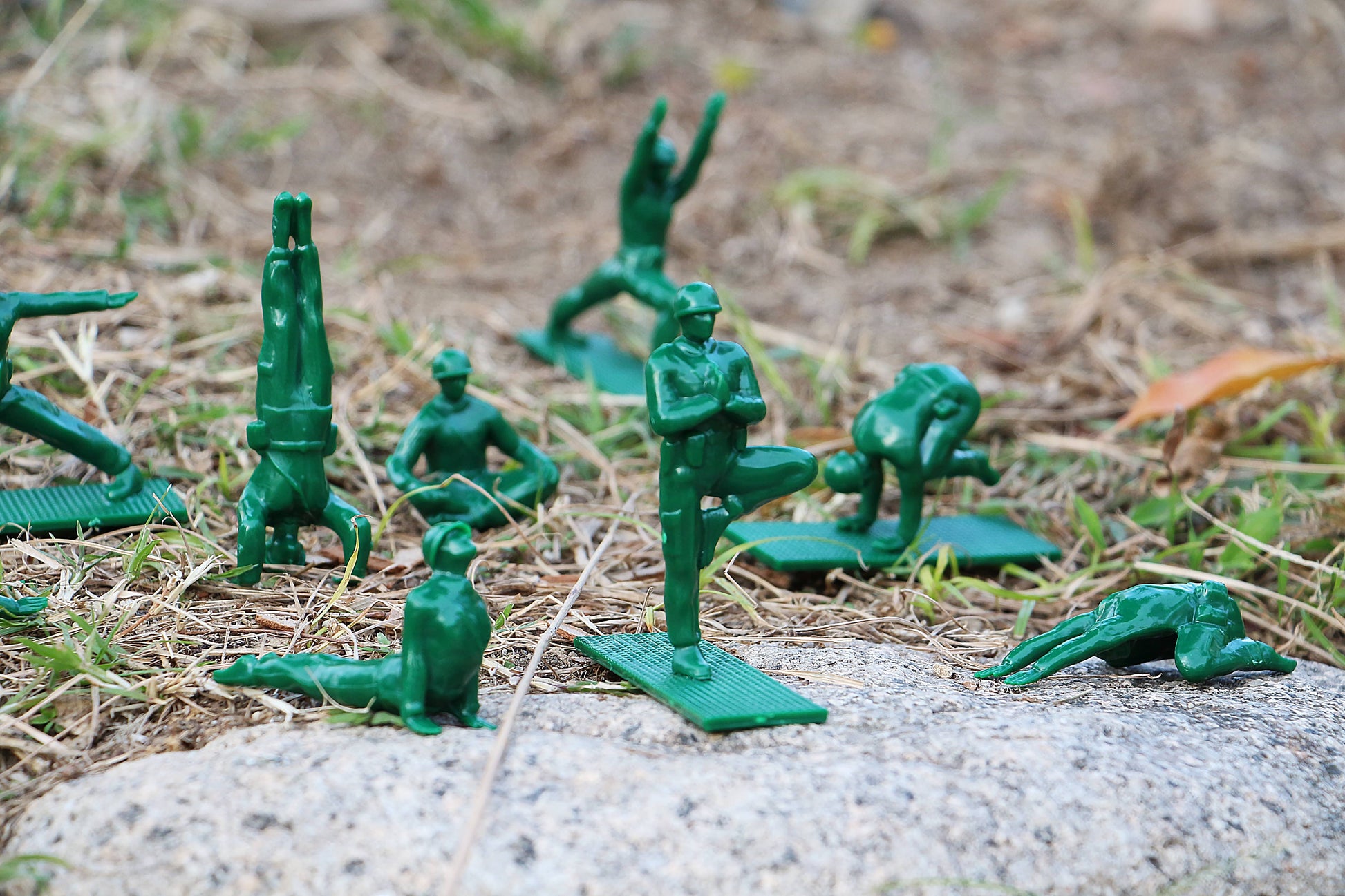 DETAIL Yoga Joes 9 Figures by DETAIL feature green plastic toy soldiers posed in various yoga positions outdoors on grass and rocks, each on a small mat, imitating yoga poses instead of traditional military stances.