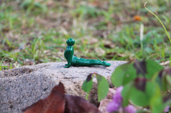 A DETAIL Yoga Joes 9 Figures figurine by DETAIL, in a green cobra pose, is set on a rock outdoors with blurred grass and plants in the background.