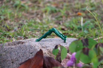 A DETAIL Yoga Joes 9 Figures toy soldier in green is posed crawling on a rock among grass and leaves outdoors.