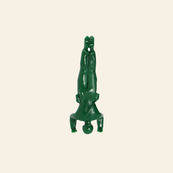 A DETAIL Yoga Joes figure from the DETAIL Yoga Joes 9 Figures set, made of green plastic, does a headstand with arms bent and legs together on a plain beige background.