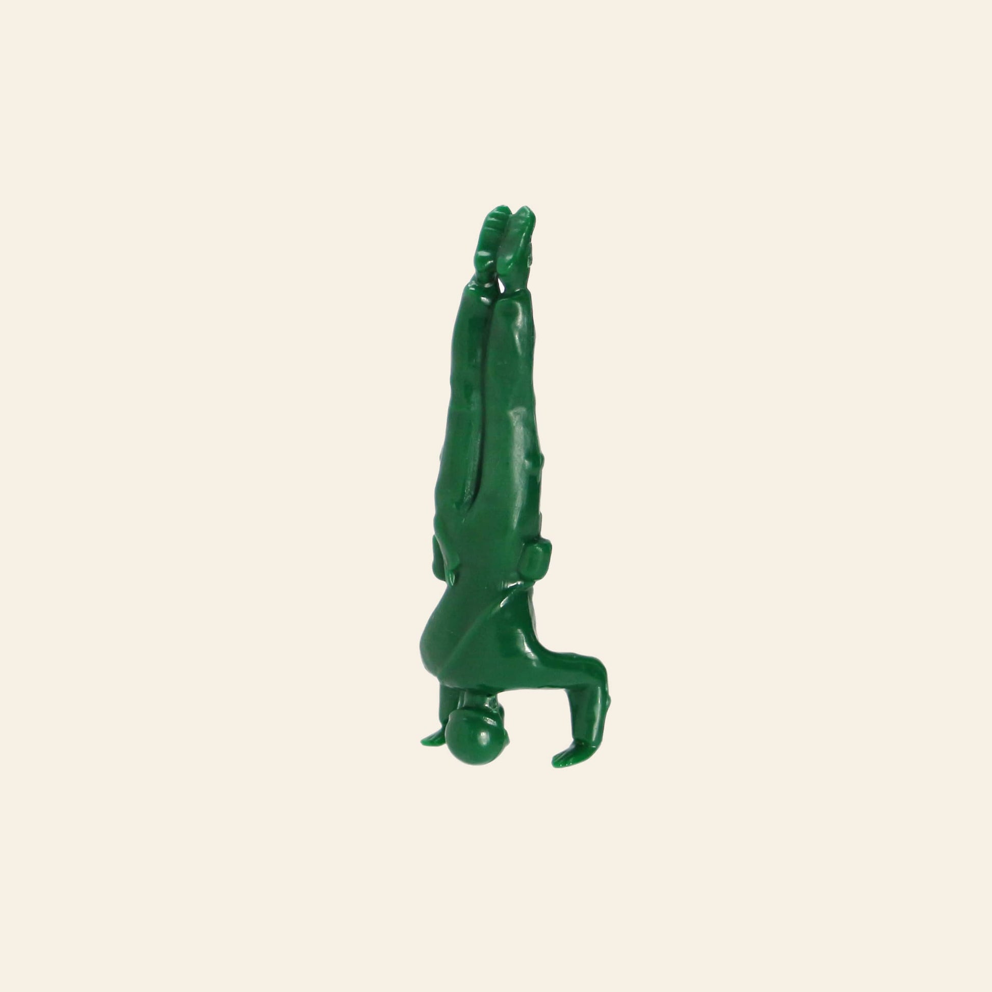 A DETAIL Yoga Joes 9 Figures green plastic toy soldier is balanced upside down on its head, legs straight up and arms bent, shown against a plain beige background.