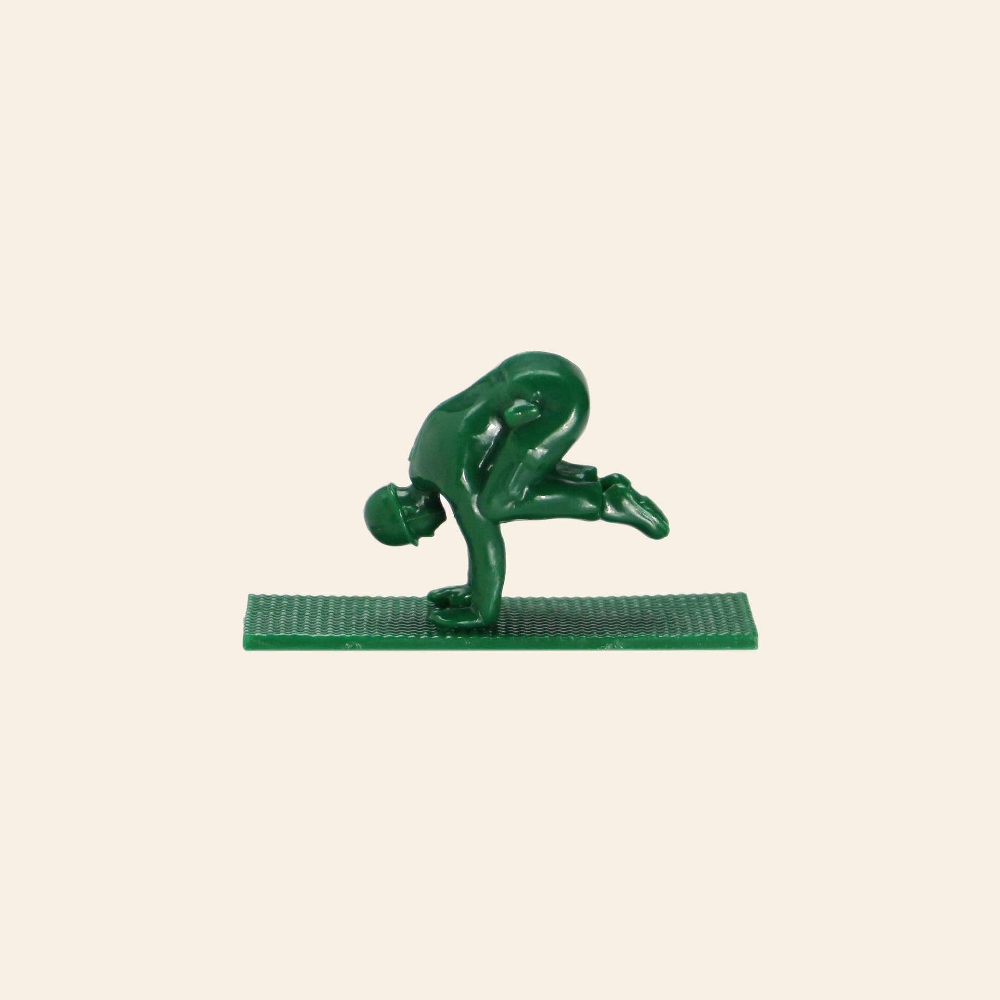 A DETAIL Yoga Joes 9 Figures toy soldier by DETAIL, in green, balances on its hands with bent legs and one knee on an arm, posed on a rectangular base against a plain light background.